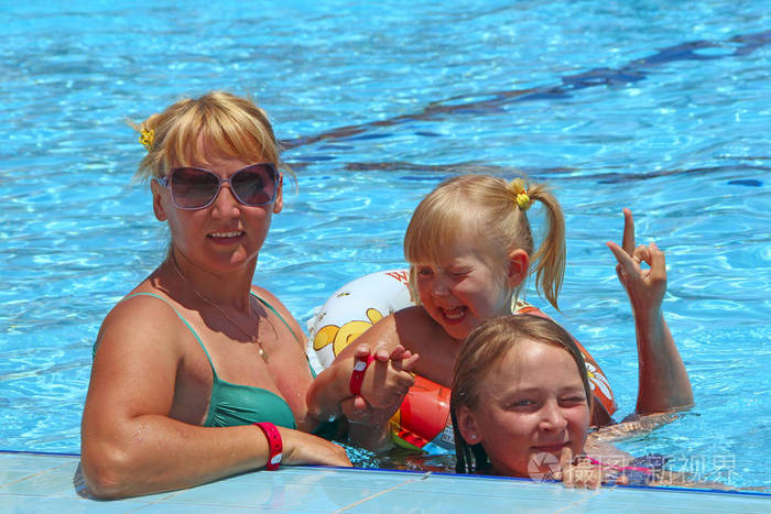 快乐的母亲和她的女儿坐在游泳池里，在镜头前摆姿势。 快乐的家庭团队。 享受暑假的家庭。 享受家庭假期的人。 女性团队