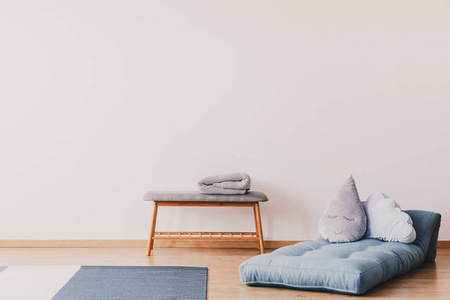 蓝色床垫，可爱的枕头在地板上的时尚婴儿房内部，复制空间在空的白色墙壁和木制和灰色与灯