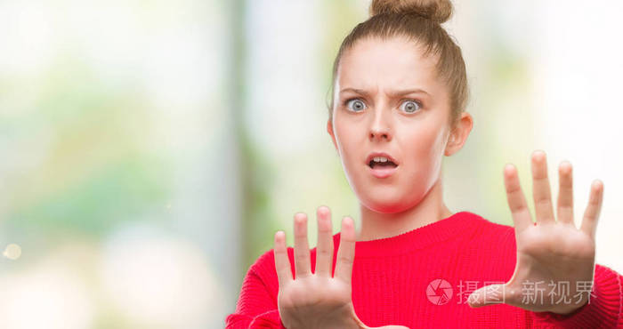 年轻的金发女人戴着发髻和红色毛衣,害怕和害怕,表情恐惧,停止用手做