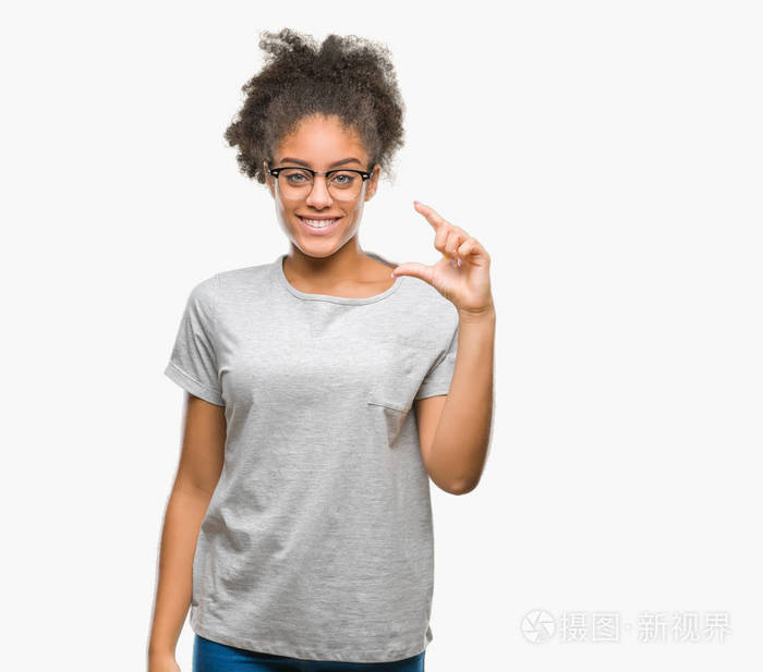 年轻的美国妇女戴着眼镜在孤立的背景上微笑和自信的手势，用手做大小标志，同时看和相机。衡量概念。