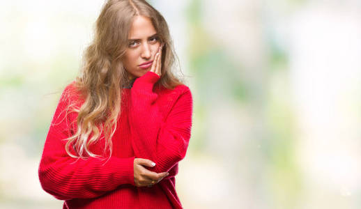 美丽的年轻金发女人穿着冬天的毛衣，在孤立的背景下思考，看起来疲惫，厌倦了交叉双臂的抑郁问题。