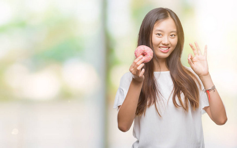 年轻的亚洲女性在孤立的背景下吃甜甜圈