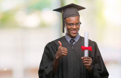 年轻毕业的非裔美国人，在孤独的背景下保持着学位，开心地大笑着做着好的标志，用手指竖起大拇指，很棒的标志