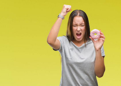 年轻的白种人女人在孤立的背景下吃甜甜圈，愤怒和沮丧地大喊大叫，疯狂地举起手大喊大叫，愤怒的概念