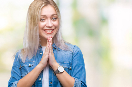 年轻的金发女人在孤立的背景下祈祷，双手一起请求宽恕，微笑自信。