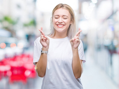 年轻的金发女人在孤立的背景上微笑着交叉手指与希望和眼睛闭上。运气和迷信观念..