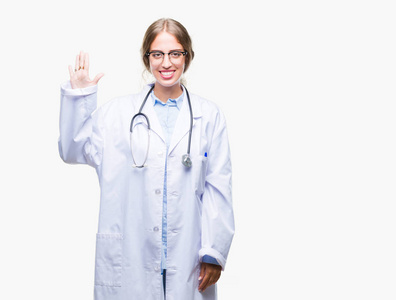美丽的年轻金发医生女人穿着医疗制服，在孤立的背景上，显示和指着第五个手指，同时微笑自信和快乐。