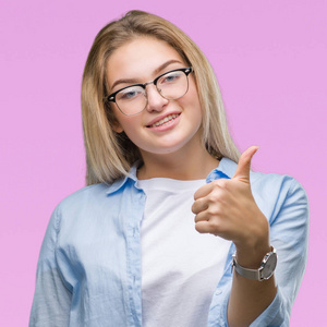 年轻的白种人商业女性戴着眼镜，在孤立的背景下，用手做着快乐的竖起大拇指的手势。赞许的表情看着相机，显示出成功。