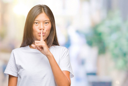 年轻的亚洲女人，在孤立的背景上要求安静，手指在嘴唇上。 沉默和秘密的概念。