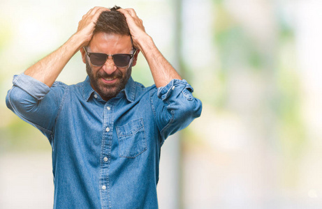 成年西班牙裔男子戴着太阳镜，在孤立的背景下患有头痛，绝望和压力，因为疼痛和偏头痛。 手放在头上。