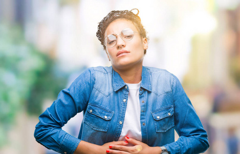 年轻的辫子非裔美国女孩戴着眼镜,戴着孤立的背景,手放在肚子上,因为