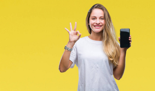 年轻漂亮的金发女郎在孤立的背景下展示智能手机屏幕，用手指做OK标志，这是一个极好的象征。