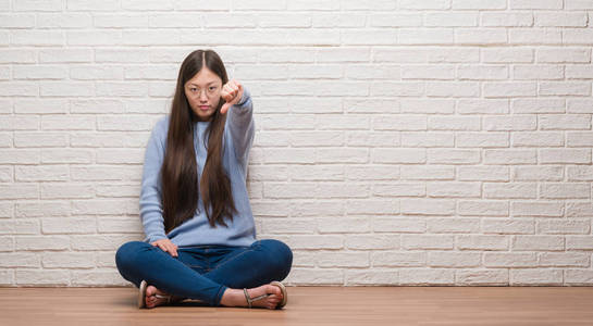 年轻的中国女人坐在砖墙上的地板上,看上去不高兴和愤怒,表现出拒绝和