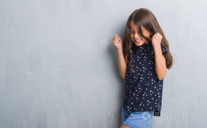 年轻的西班牙裔孩子在灰色的墙壁上,非常高兴和兴奋地做着胜利者的