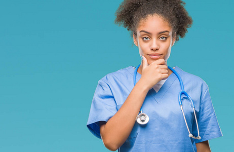 年轻的非洲美国医生女士在孤立的背景下，自信地看着相机，微笑着交叉的手臂和举起的手在下巴上。 积极思考。