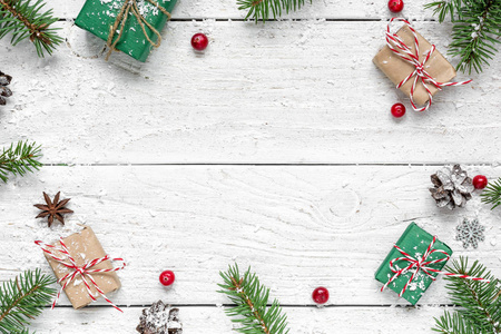 圣诞作文。 框架由冷杉枝，红色浆果，礼品盒和松果在白色的木制桌子上覆盖着雪。 圣诞背景。 平躺着。 顶部视图，复制空间