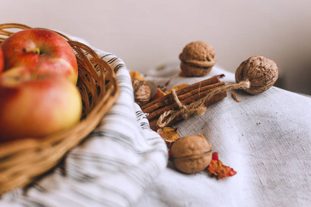 还活着的生活与苹果在柳条篮子站在条纹亚麻织物, 核桃, 花瓣和肉桂棒包裹在绳子。秋季和秋季感恩节贺卡制作概念