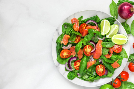 新鲜沙拉与鲑鱼菠菜，樱桃，西红柿，红洋葱和罗勒在大理石盘子在白色大理石桌子上。 健康的食物概念。 顶部视图，复制空间