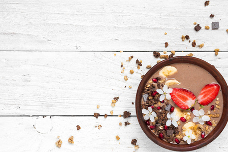 可可香蕉蛋白冰沙碗配巧克力麦片草莓和石榴籽装饰花。 顶部视图与复制空间。 健康早餐