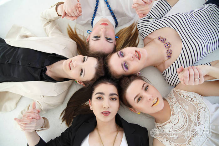 一群快乐优雅的女孩躺在一个圆圈里,白色背景上的俯视.照片-正版商用