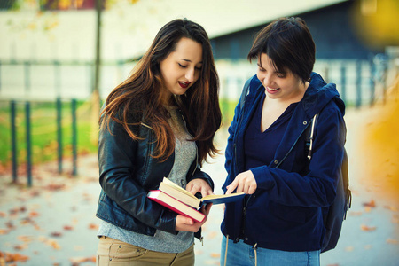 两个开朗的年轻女学生手指着一本书，为他们的问题找到正确的答案。 教育是解决生活问题的办法。 团队合作和友谊的概念。