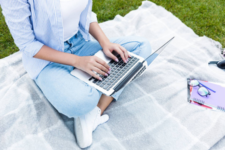 使用笔记本电脑在公园户外拍摄的年轻女人的照片。