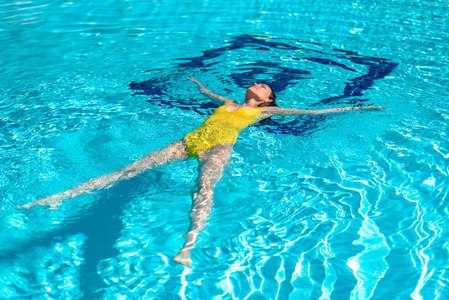 穿黄色泳衣的女人躺在游泳池里的水上，明星放松放松健康。
