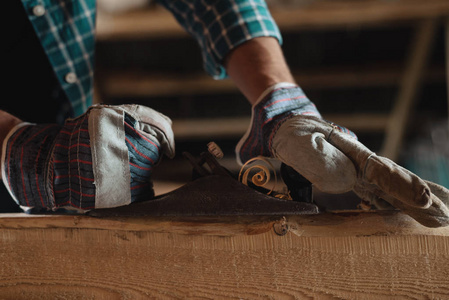 s hands in working gloves with hand plane cut wood. woodworking