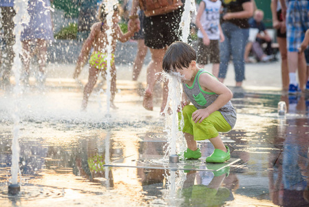 兴奋的男孩在喷泉里的喷水之间玩得很开心。 城市里的夏天。 孩子快乐的笑脸。 生态概念。
