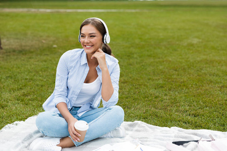 美丽的年轻美丽的女人在公园户外听音乐喝咖啡。