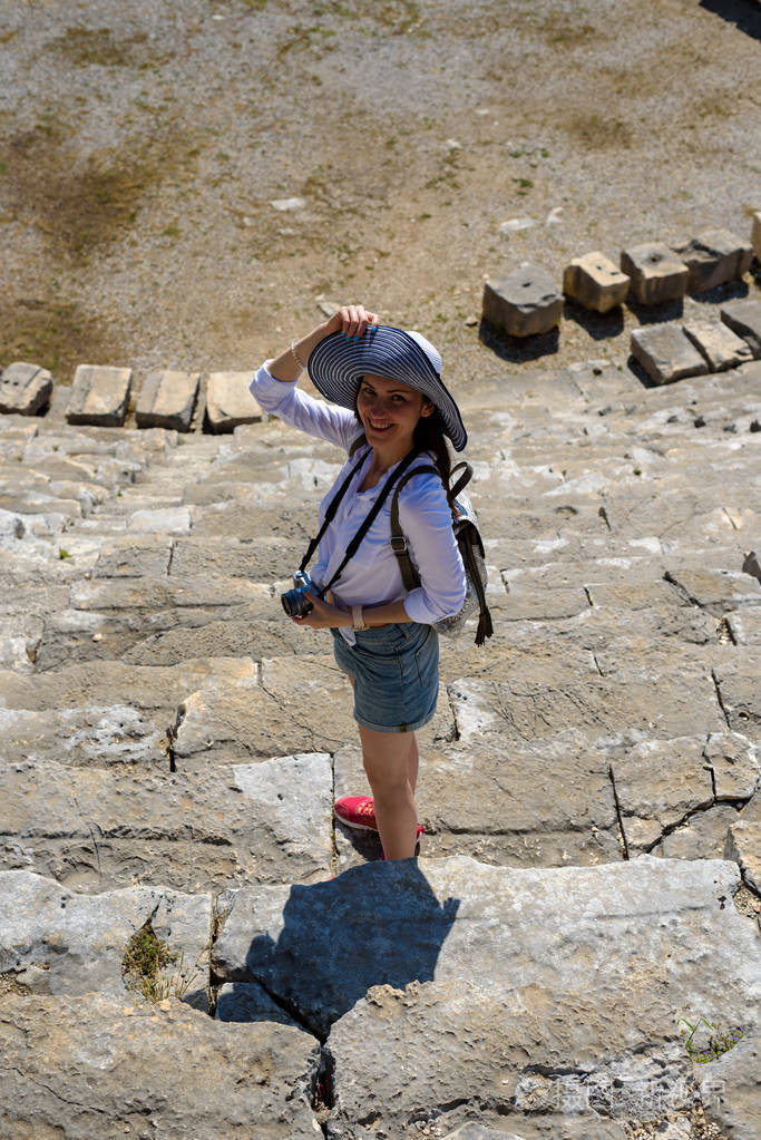 年轻微笑的女人戴着帽子，手里拿着相机，在远足建筑圆形剧场旅行者休闲。