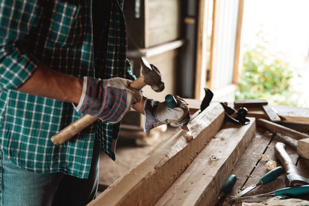 木匠用锤子和凿子处理木材。 工人在车间工作。 他们的手在家里的作坊
