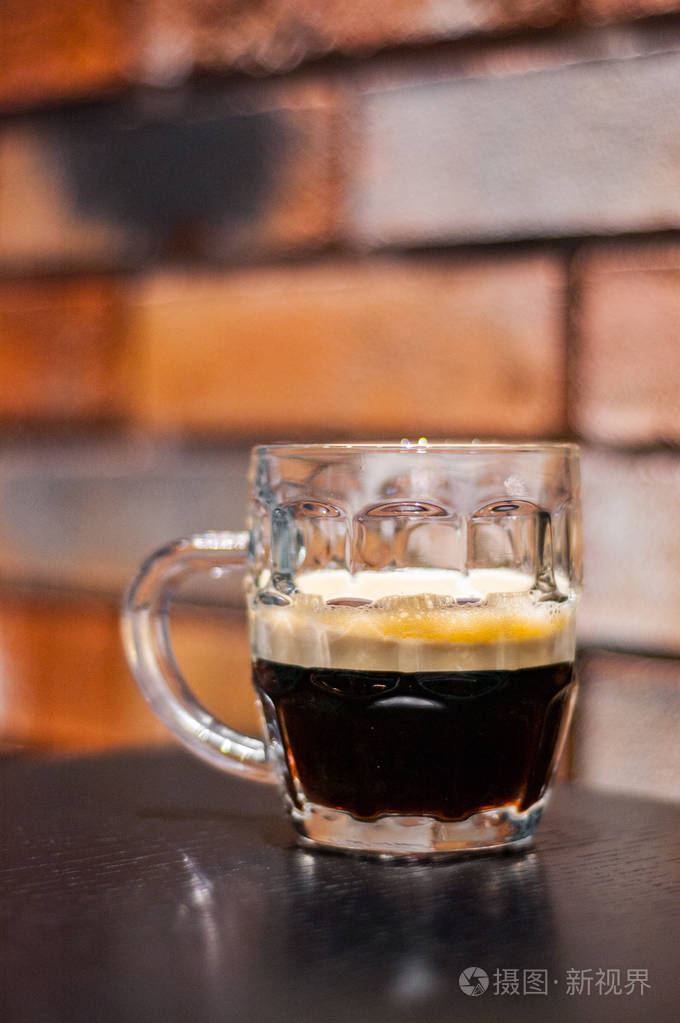 在砖墙背景上的酒吧里的木桌上用一杯深色啤酒