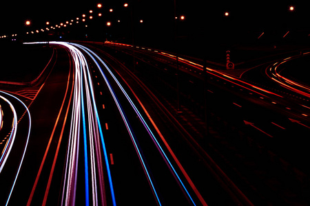 夜晚，汽车在弯曲的高速公路上照亮小径。夜间交通通道。动作模糊。夜间城市道路与交通前照灯运动。城市景观。通过车辆运动模糊来点亮道路