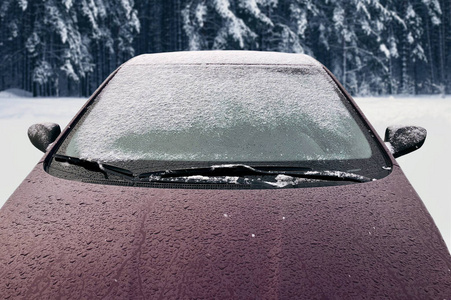 冰雪覆盖的冬季汽车，可以在雪地背景上看到前窗挡风玻璃和引擎盖