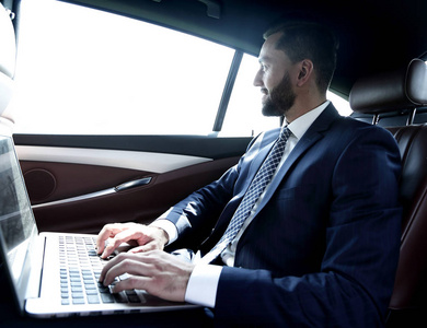 坐在车里同时在笔记本电脑上键入文本的商人