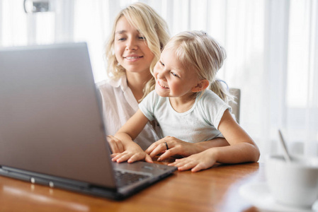 微笑的母亲和孩子在家里使用笔记本电脑。 父母在一起的感觉幸福的家庭