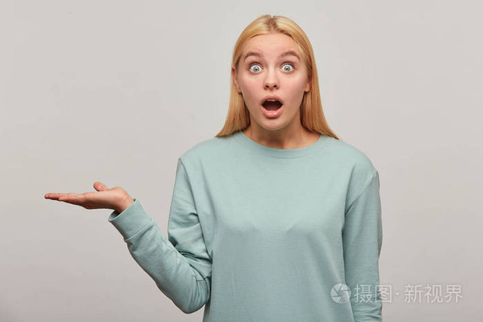 令人震惊的金发女郎惊讶地睁大眼睛,张开嘴,一只手捧着铜空间,穿着