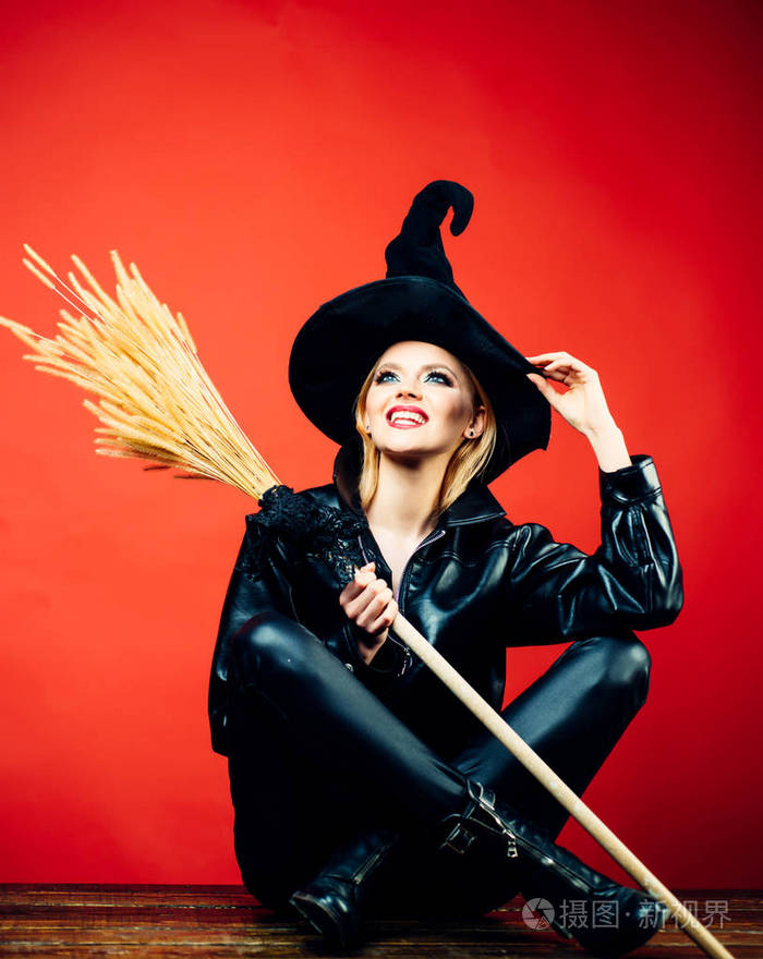 情感年轻妇女在万圣节服装在党在红色背景与南瓜.女巫拿着扫帚或扫帚