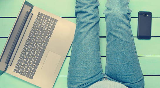 现代女孩坐在蓝色的木制地板上，用笔记本电脑。 一代Z.自由职业者的概念。 工作空间。 上面的风景。