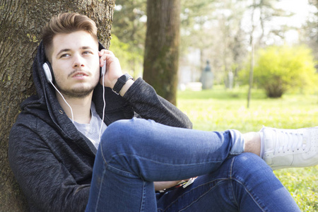 英俊的年轻人喜欢在户外听音乐。 选择性聚焦和小的景深。