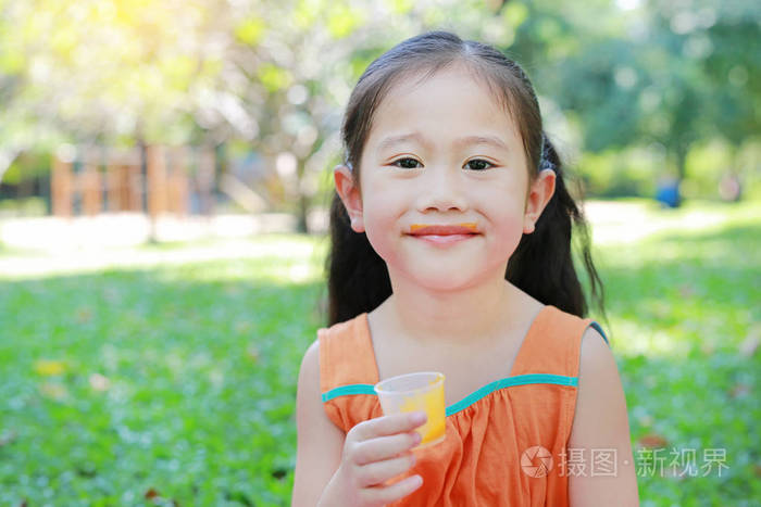 小女孩在夏天的花园里喝着橙汁，嘴上沾满了橘子汁。