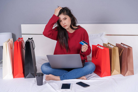压力大的妇女在床上使用笔记本电脑进行网上购物，并有信用卡阻塞的问题