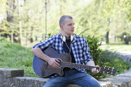 英俊的年轻人拿着吉他享受公园。选择性的焦点和小的景深。