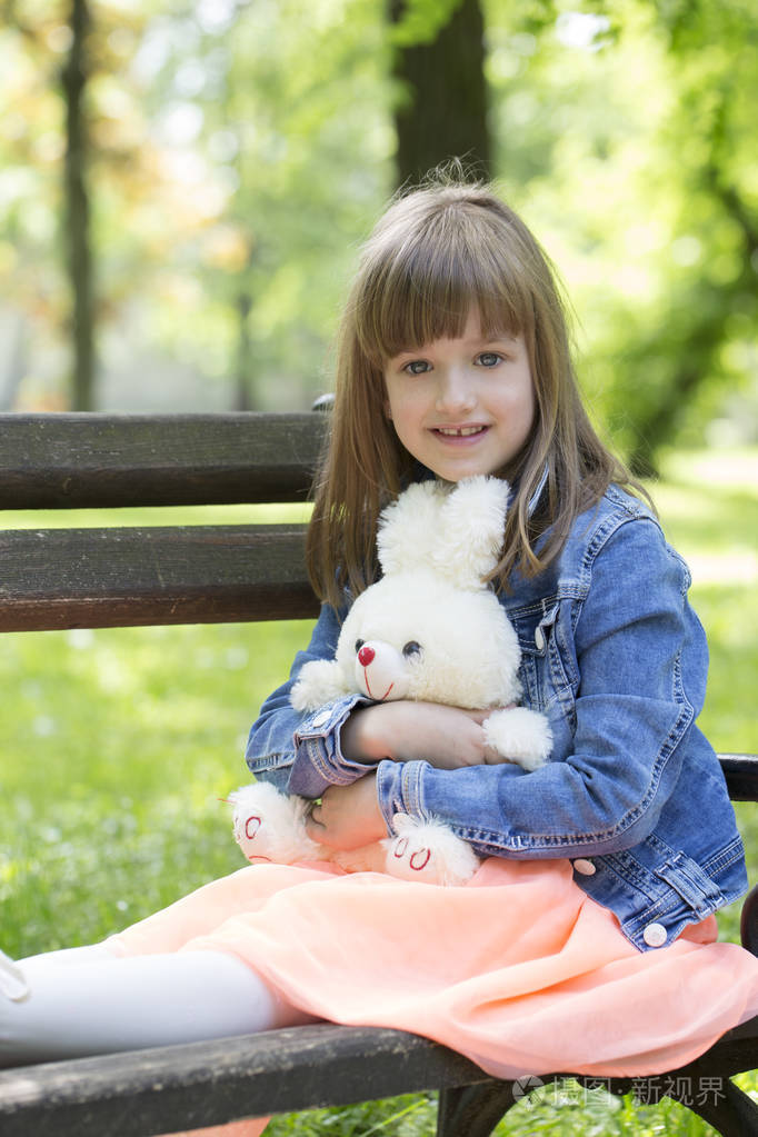 小女孩坐在公园的长凳上,手里拿着她最喜欢的毛绒玩具