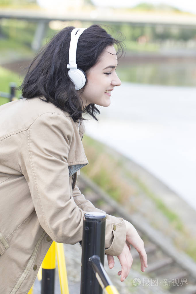 年轻的美女站在河边听音乐享受着