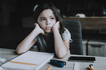 小女孩坐在桌子旁,表现出无聊的表情.