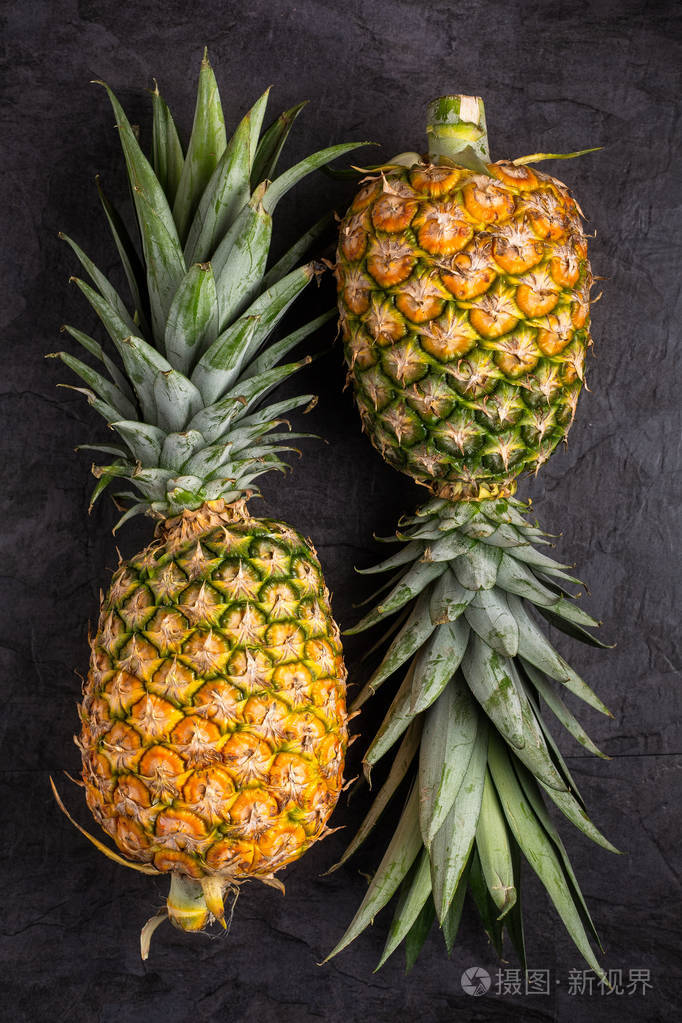 两个新鲜的成熟菠萝，深色背景，垂直构图，俯视