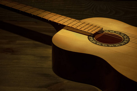 黑暗中的一束光声学吉他躺在黑暗中的木桌上,一束光照亮了它.照片