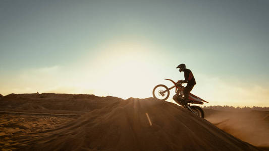 专业摩托车越野车手跳过沙丘，并进一步沿着越野赛道。 太阳落山时在荒无人烟的采石场开枪。